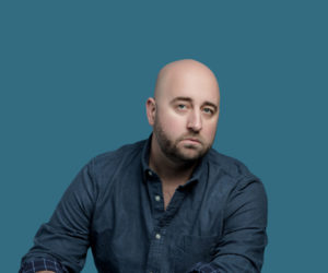 Luke posed in front of a blue background wearing a navy shirt